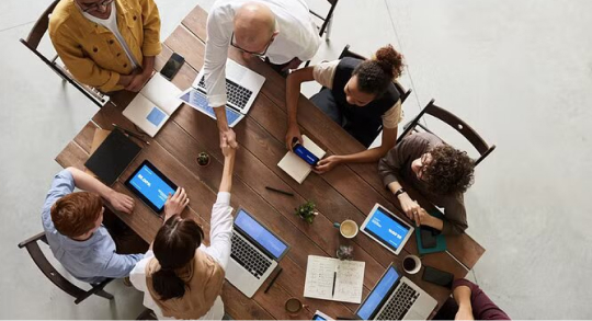 A diverse group of professionals collaborates around a table, each using laptops in a modern office setting.
