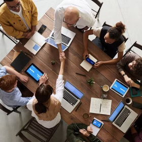 Blog thumbnail: A diverse group of individuals collaborating around a table, each using laptops.
