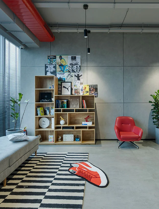 Contemporary room with a bookshelf, red chair, striped rug, sneaker decor, and Puma-themed wall posters in a modern setting.