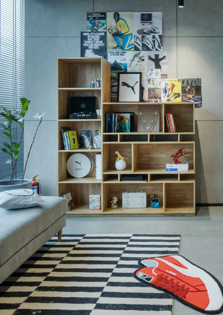 Contemporary room with a bookshelf, red chair, striped rug, sneaker decor, and Puma-themed wall posters in a modern setting.